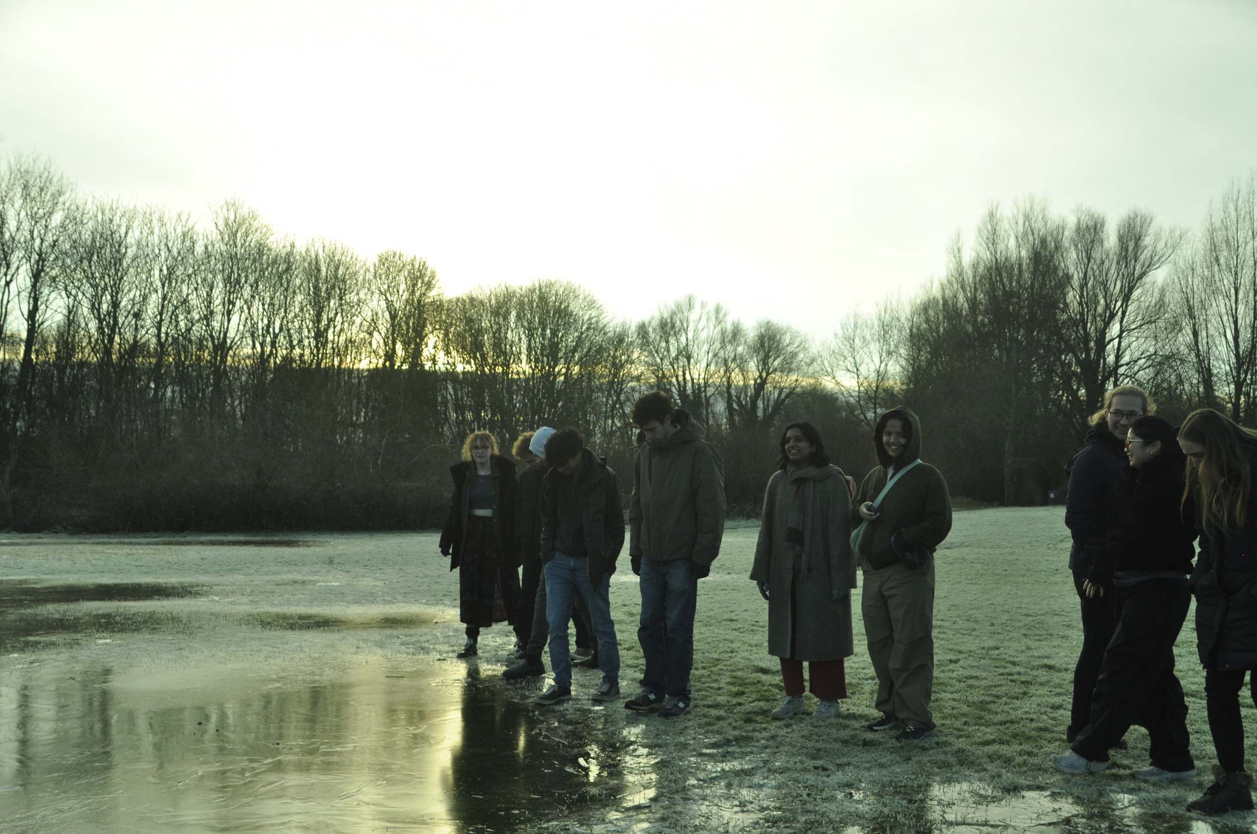 A group of OAISI members on a frosty field at dusk, gathered around a frozen puddle